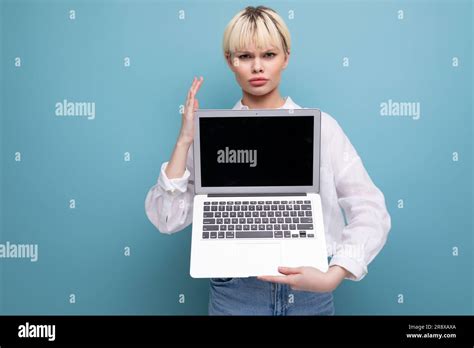 jeune femme blanche blonde avec une coupe courte vêtue d une chemise blanche et un jean tient un