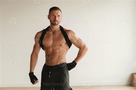 An Adult Muscular Man With A Naked Torso Stands In A Room On A Light