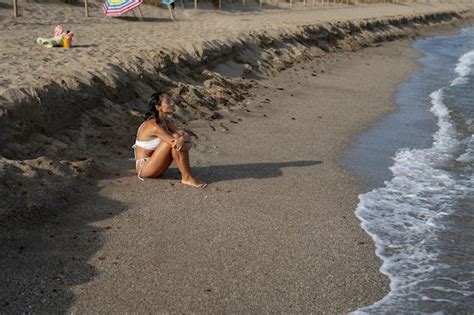 Premium Photo Beautiful Brunette Girl In A White Swimsuit Sits On The Sand On The Seashore