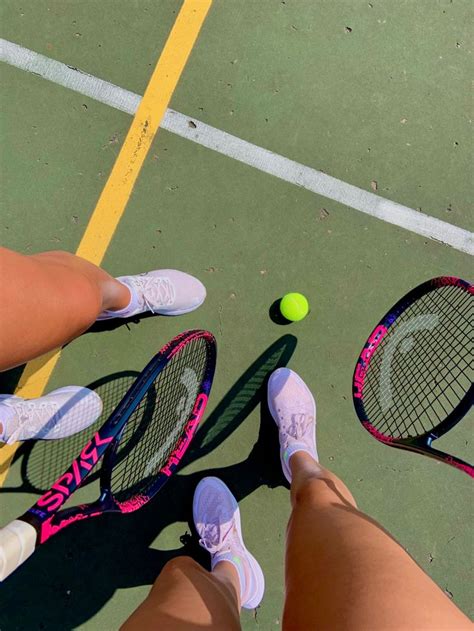 Two People Standing On A Tennis Court Holding Racquets Next To Each Other