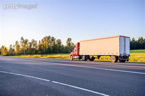 Red Big Rig Day Cab Semi Truck Transporting Cargo In Dry Van Semi