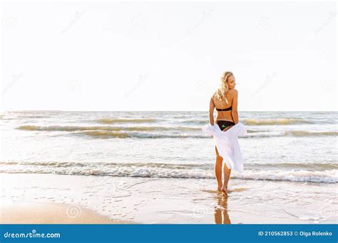 Beautiful Blonde Slim Woman Wearing Black Bikini And White Shirt On The Beach Of Sea Or Ocean