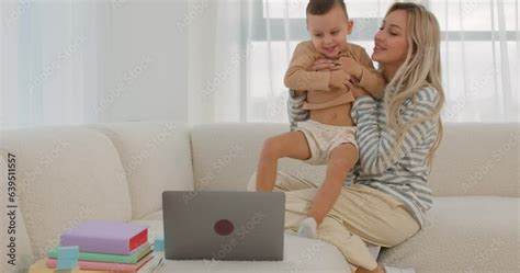 Awesome Blonde Mom With Infant Son On Knees Using PC Computer In Living