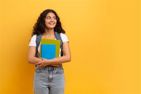 Estudante indiana sorridente segurando cadernos olhando para o espaço