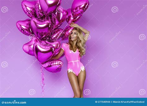 Fille Blonde Sexy En Costume De Latex Rose Tient Des Ballons Roses Sur Fond Lilas Et Pose