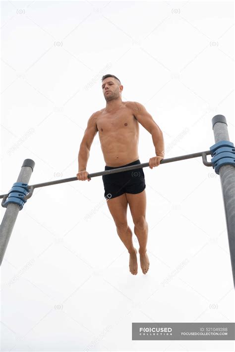 Low Angle Of Muscular Male Athlete With Naked Torso Doing Chin Ups On Horizontal Bar During