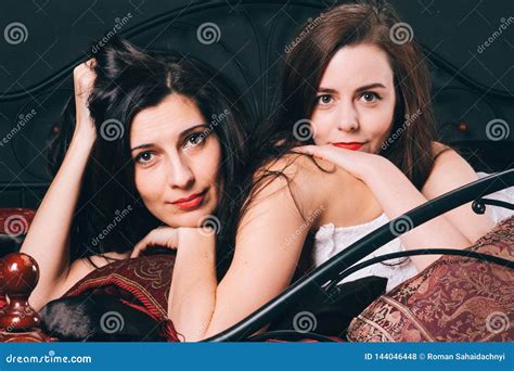 Twee Jonge Vrouwen In Uitstekende Lingerie Op Het Verspreidingsbed Tegen De Zwarte Muur