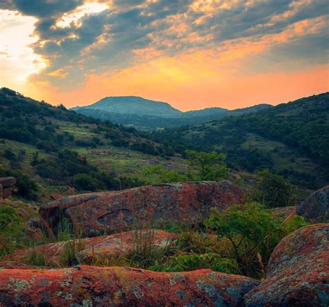 the sun is setting over some rocks and trees with mountains in the ...