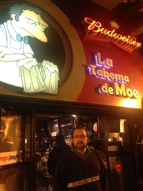 A Man Standing In Front Of A Bar With Neon Signs On The Wall Behind Him