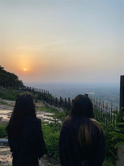 two people are sitting on a bench watching the sun go down over a valley and hills