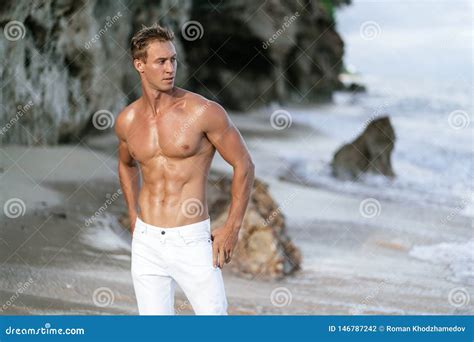 Muscular Athletic Man In White Pants With A Naked Torso On The Beach