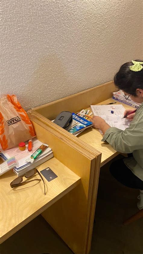 A Woman Sitting At A Desk Writing On A Piece Of Paper Next To A Bag