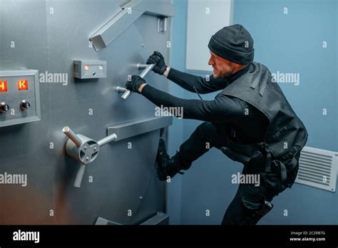 Bank robbery, male robber in black uniform trying to break vault lock ...