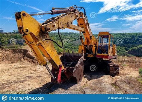 Yellow Excavator During Earthmoving At Open Pit On Blue Sky Background