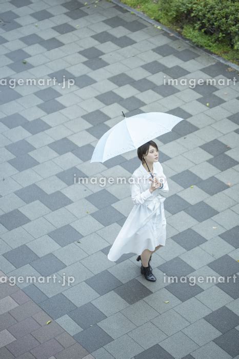 雨の中傘をさして歩く白いワンピースを着た若い女性の写真素材 164115627 イメージマート