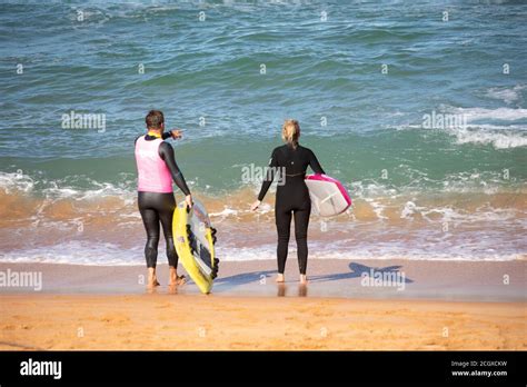 Man And Woman Wearing Wetsuits On The Beach With Their Surfboards