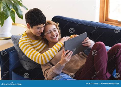 Happy Biracial Lesbian Couple Embracing On Couch Using Tablet At Home Stock Image Image Of