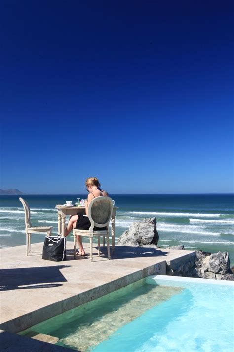 A Woman Sitting At A Table Next To An Empty Pool On The Beach Near The