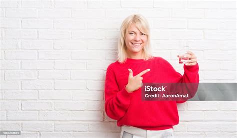 Adult Caucasian Woman Over White Brick Wall Drinking A Glass Of Water