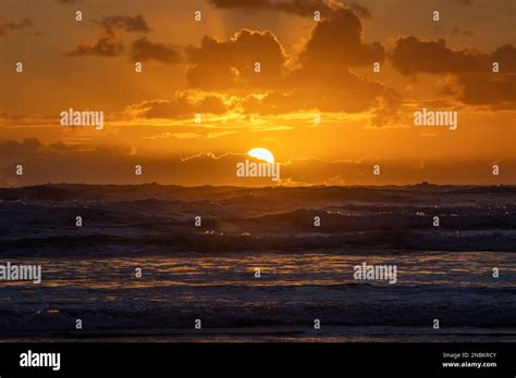 A Dramatic Orange Sunset Peeking Out From Behind A Layer Of Clouds