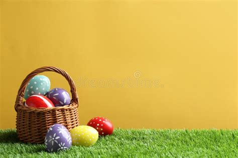 Wicker Basket With Painted Easter Eggs On Green Grass Against Color