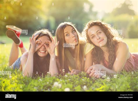 Three Beautiful Girls Laughing Together And Lying On Grass Outdoors In