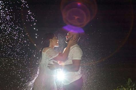 A Man And Woman Standing In The Water At Night With Their Arms Around