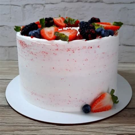 A White Cake Topped With Fresh Fruit On Top Of A Wooden Table Next To A