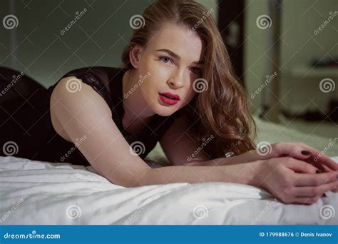 A Very Brunette With An Alluring Look Poses In Erotic Black Lingerie On A Straightened Bed Stock