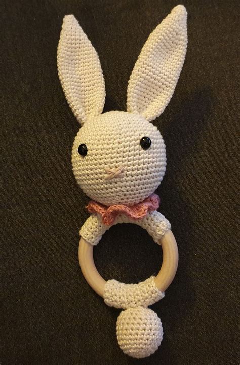 A Crocheted Bunny Ring Rattler On A Black Surface With A Pink Bow Tie