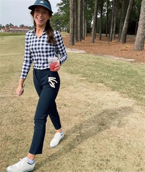 a woman walking across a grass covered field holding a drink in one hand and a frisbee in the other