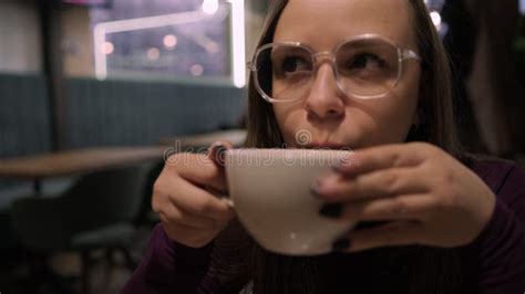 A Woman Is Seated At A Table Holding A Cup Of Coffee In The Cafe She