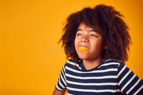 Studio Portrait Of Smiling Boy Pulling Funny Face With Orange For Mouth