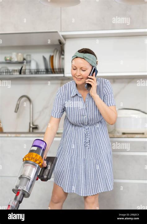 Housewife is cleaning the room - vacuuming and talking on smartphone at