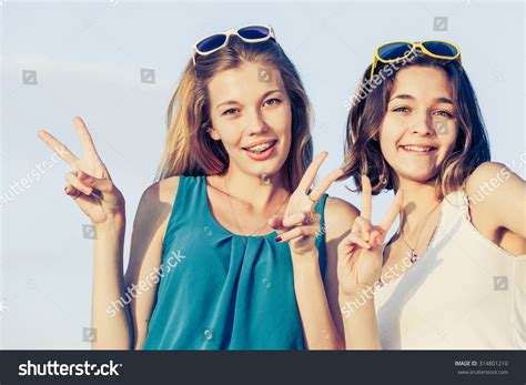 Pretty Beautiful Brunette And Blonde Girl Friends Having Fun Both Standing In Park And Smiling