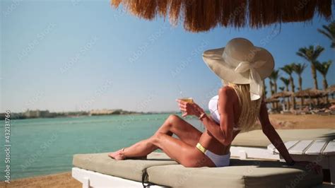 Sexy Woman Wearing Bikini Sitting On Lounger Under Straw Canopy