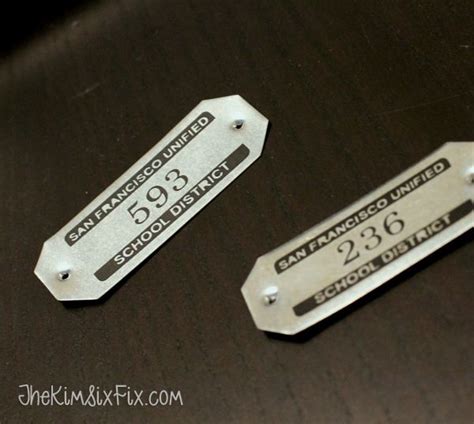 two metal tags sitting on top of a wooden table next to each other with ...