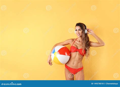 Mujer Atractiva Bonita En Bikini Elegante Con Los Auriculares Y La Pelota De Playa En Fondo Del