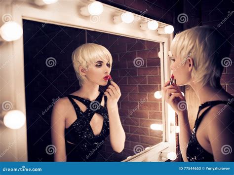 Beautiful Blonde Woman Looking Into A Mirror At Herself And Applying Red Lipstick Stock Image