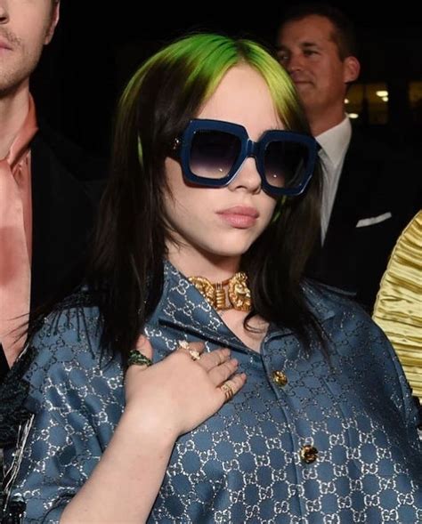 A Woman With Green Hair Wearing Sunglasses And A Blue Dress Is Standing