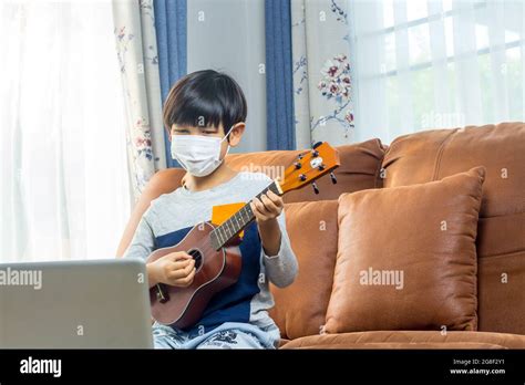 A boy wearing a face mask plays ukulele in front of a laptop Stock Photo - Alamy