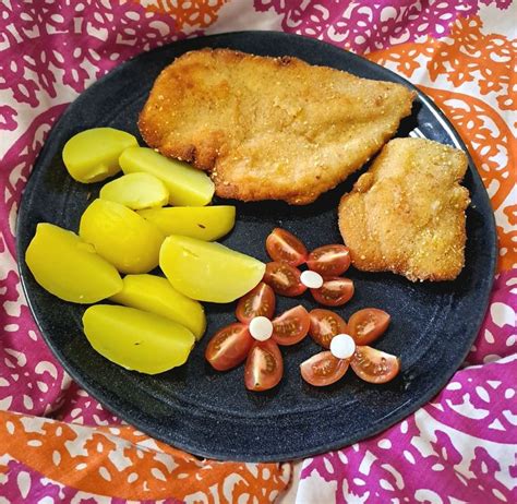 A Black Plate Topped With Fish Potatoes And Carrots On Top Of A