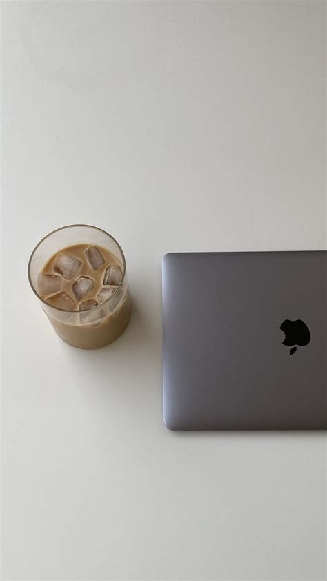 An Apple Laptop Sitting Next To A Drink On A White Counter Top With A