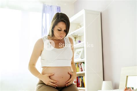 Portrait Of Beautiful Pregnant Woman Holding Her Belly In Bedroom