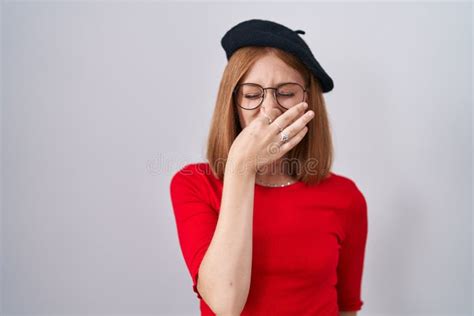 Young Redhead Woman Standing Wearing Glasses And Beret Smelling