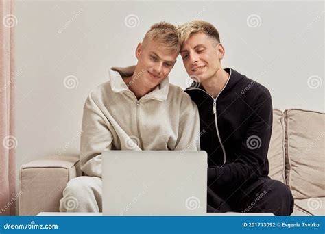 Gay Couple Of Men In Pajamas On The Couch And Looking At The Laptop Screen Stock Photo Image