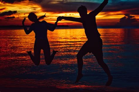 Silueta De Una Pareja Saltando En La Playa Contra El Cielo Durante La