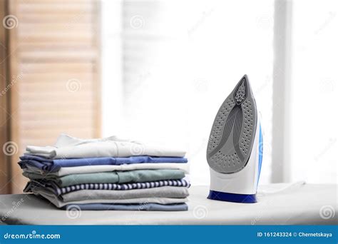 Board With Modern Iron And Stack Of Clothes Laundry Day Stock Photo