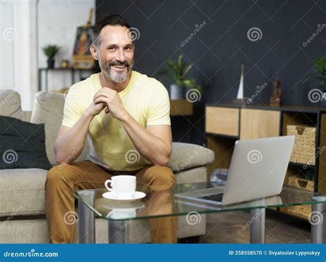 Smiling Middle Aged Man Sitting On Sofa Couch Drinking Coffee While