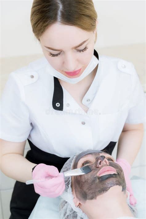 The Cosmetologist In Pink Gloves With A Brush Applies A Carbon Mask For